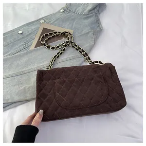 Brown quilted velvet crossbody bag with metal chain strap on a white bedding scene