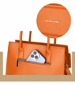 Detail of orange handbag showing the metal logo, stitching, and front zipper pocket