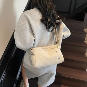 Detail of a beige canvas shoulder bag with wide branded straps worn on a casual outfit