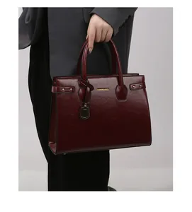 Detail of wine red tote bag with polished finish, gold logo, and metallic rivet studs