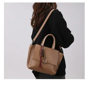 Detail van bruine tas met litchi-textuur en hanger getoond op een modelrugzijde