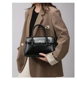 Détail d'un sac cabas en cuir brillant noir avec anse tressée et fermoir rotatif argenté