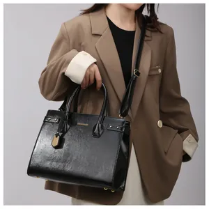 Close-up of black glossy leather tote featuring gold rivets and detachable shoulder strap