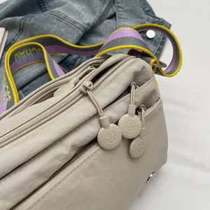 Detail of beige nylon crossbody bag featuring multi-layer zippers and colorful striped strap