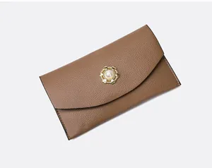 Detail van bruine enveloppeclutch met lychee leerstructuur en gouden parel hartsluiting