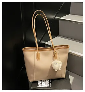 Detail of a beige tote bag with brown trim and a white plush pom-pom charm on steps