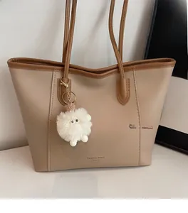 Detail of soft beige tote bag with brown handles and plush monster charm on a white table