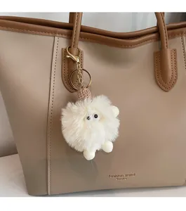 Close-up of white fluffy plush charm with gold metal clasp on a stylish bucket bag
