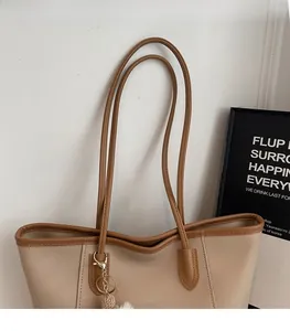 Detail of minimalist tote bag with thin brown straps and a decorative plush charm