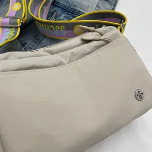 Detail of canvas shoulder bag showing wide colorful woven strap and metal logo