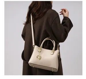 Detail der beigen Handtasche mit goldfarbenen Beschlägen und Rosenblüten-Anhänger