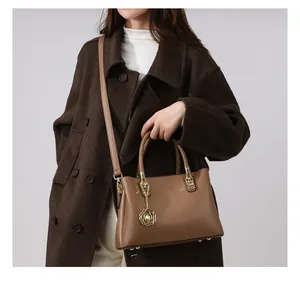 Detail einer braunen Ledertasche mit goldenem Kamelienanhänger und dünnem Schultergurt