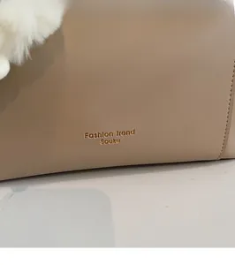 Close-up of beige leather bucket bag with gold logo and white plush pom-pom charm