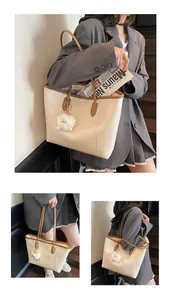 Detail of cream tote bag featuring brown leather trim and a cute plush monster charm
