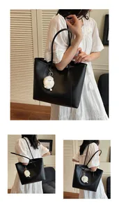 Close-up of black leather tote bag with minimalist strap and white plush sheep charm