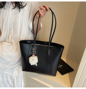 Detail of black leather tote bag with Fashion Trend logo and white plush charm on model
