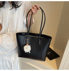 Detail of black faux leather tote bag featuring a cute white plush eye charm and thin straps
