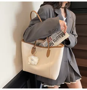 Detail of beige and brown leather tote bag with a white fluffy keychain on a model