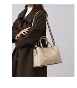 Detailansicht der beigen Lederhandtasche mit goldenem Blumenanhänger an einem Modell