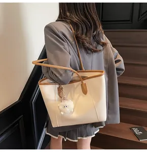 Detailed view of cream leather tote bag with brown trim and plush monster charm on model