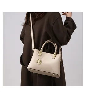 Detail einer beigen Handtasche mit Litschistruktur, Goldrosenanhänger und Bodennägeln