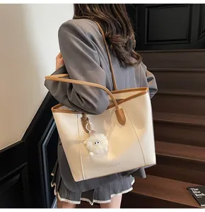 Detail of cream leather tote bag with brown trim and plush charm worn by a model