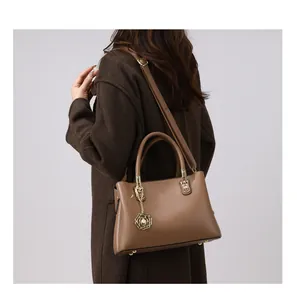 Detail der braunen Handtasche aus genarbtem Leder mit elegantem Blumen-Perlen-Anhänger
