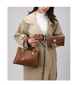 Dreiteiliges braunes Handtaschen-Set mit Tragetasche und Geldbörsen am Modell im Trenchcoat