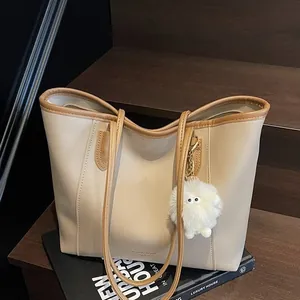 Large beige tote bag with camel straps and plush charm on a wooden background