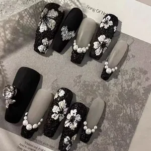 Detail of handmade press-on nails featuring black relief flowers and pearl accents