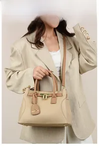 Sac bandoulière beige et marron avec cadenas doré porté par un mannequin en tailleur