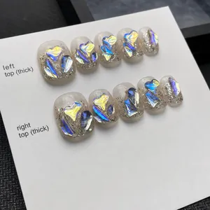 Detail of handmade press-on nails with shimmering pink base and holographic heart rhinestones
