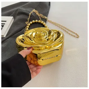 Detail of a 3D gold rose clutch bag featuring a metallic finish and beaded handle