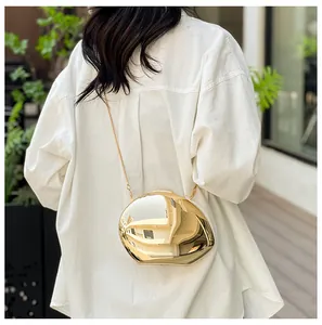 Detail of a gold metallic mirror pebble bag with an elegant chain strap on a white shirt