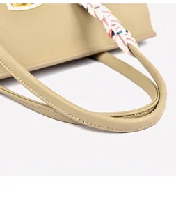 Close-up of khaki tote bag featuring gold lock and elegant silk scarf on the handle