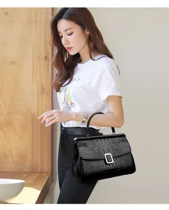 Detail of black crocodile texture handbag with silver buckle carried by a model