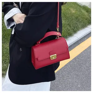 Detail of red lychee leather handbag with gold square lock worn in outdoor setting