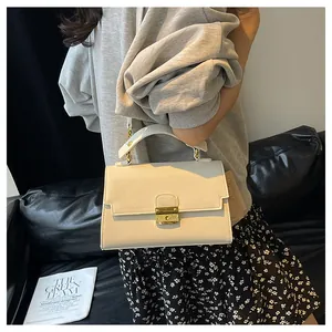 Detail of minimalist cream leather handbag featuring a square gold buckle and top handle