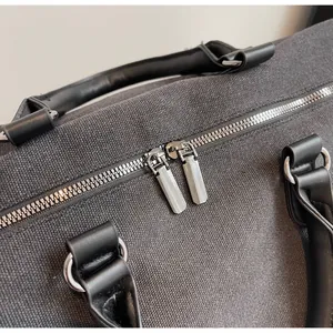 Dettaglio borsa da viaggio in tela grigia con cerniere metalliche e manici in pelle