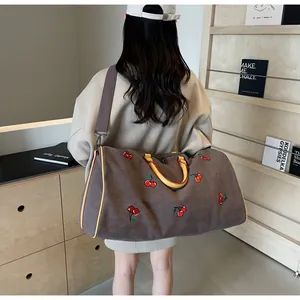 Dettaglio della borsa da viaggio vintage in tela con ricamo ciliegia e manici gialli