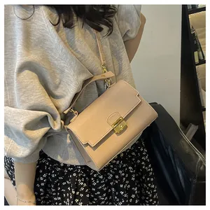Detailed view of beige leather crossbody bag with square gold lock worn by a model
