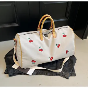 Dettaglio borsa da viaggio vintage in tela con ricamo ciliegia e manici gialli