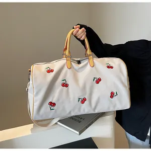 Dettaglio borsa da viaggio in tela con ricamo di ciliegie e tracolla gialla