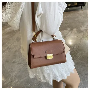 Detailed view of brown lychee-patterned leather handbag with gold metal clasp on a model