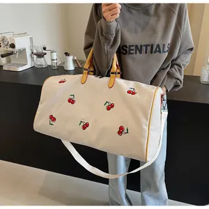 Borsa da viaggio in tela con ricamo ciliegia e manici in pelle scattata in un caffè