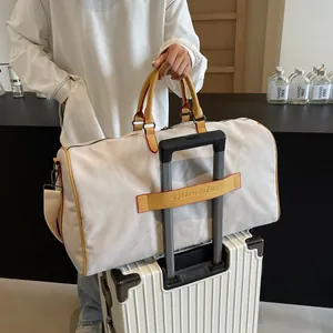 Grande borsa da viaggio vintage in tela grigio chiaro su una valigia trolley bianca