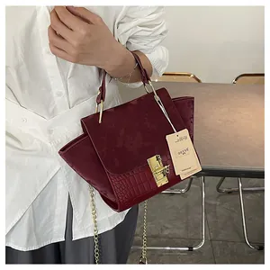 Close-up of burgundy frosted and crocodile embossed leather handbag with gold square buckle