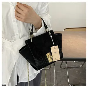 Detail of black matte suede handbag with crocodile texture and gold hardware lock