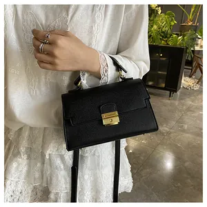 Detail of black litchi texture handbag with gold metal lock being held by a model