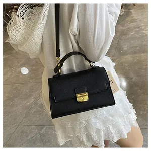 Close-up of black litchi texture handbag featuring a gold metal lock and leather handle